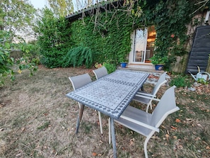 Eine Terrasse im Freien mit einem gefliesten Tisch und Stühlen, umgeben von Grünpflanzen und einem Gebäude.