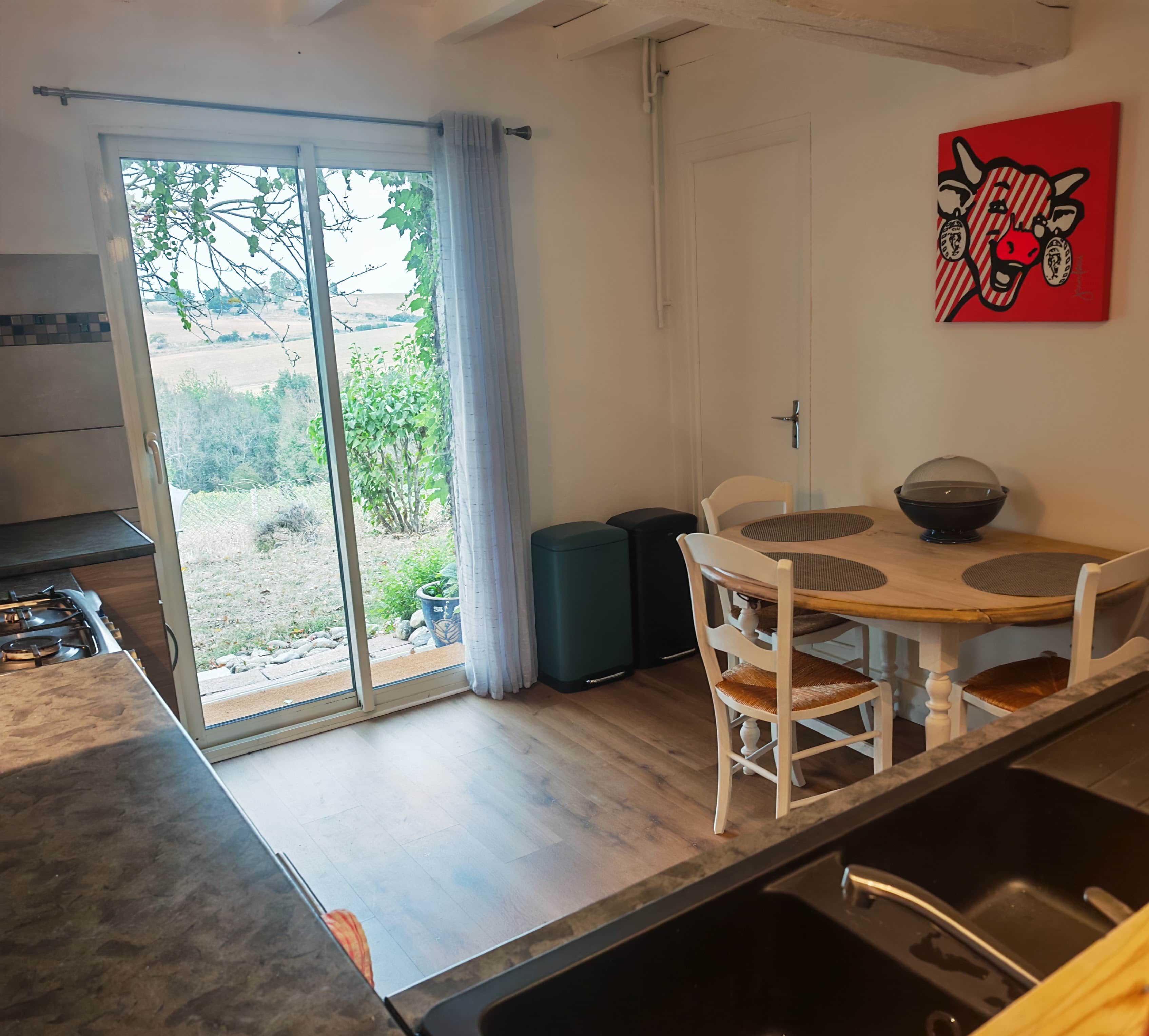 A modern kitchen with a dining area, a sliding glass door to the outdoors, and a red artwork on the wall.