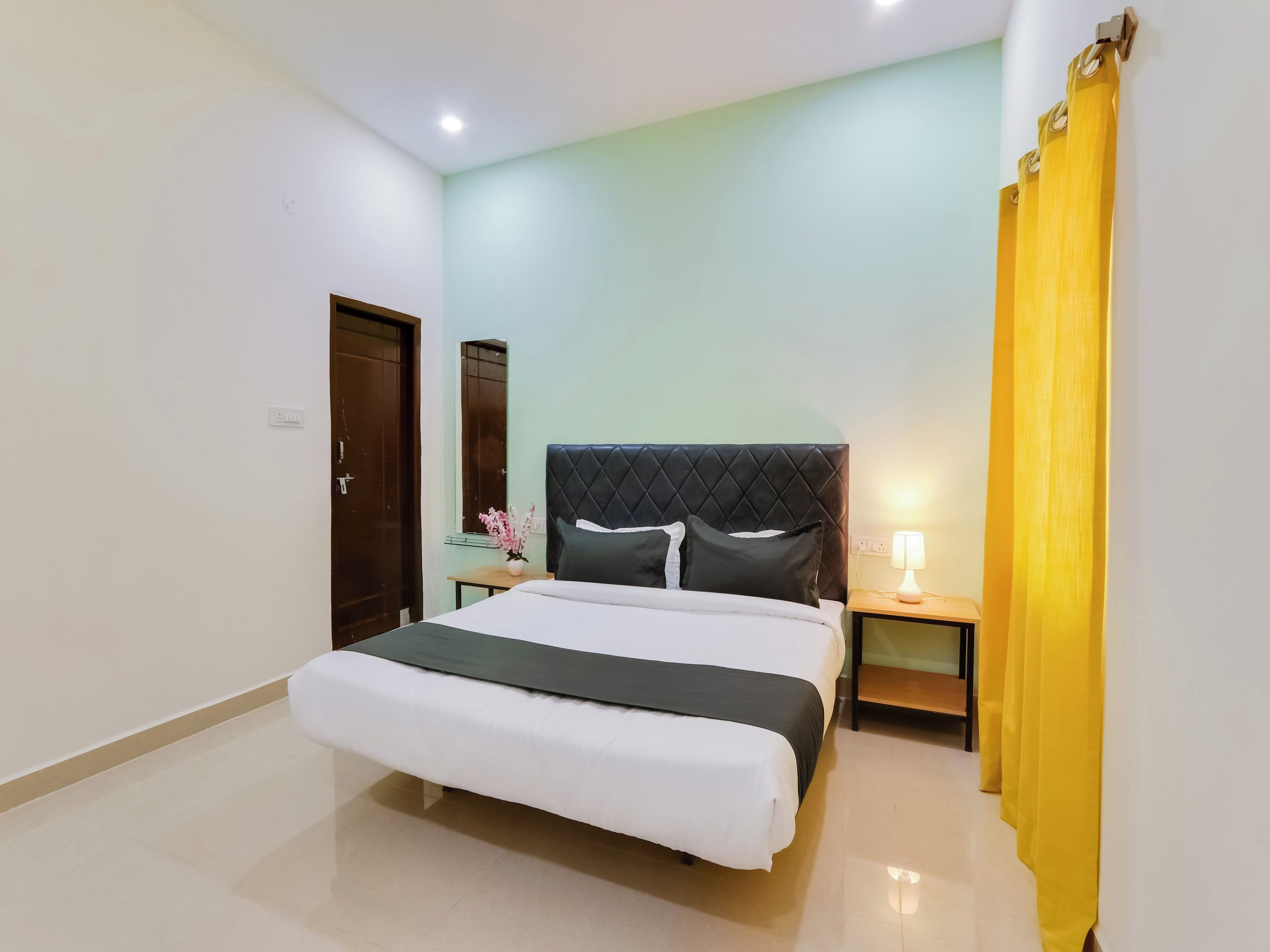 A hotel room with a bed, a nightstand, a lamp, a mirror, and a curtain.