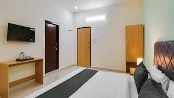 A hotel room with a bed, bedside table, TV, wardrobe, and a desk with a kettle.