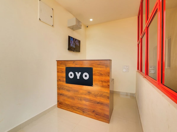 A reception desk with a sign that reads 'OYO' in a hallway with a tiled floor, a mounted television, and a window with red framing.
