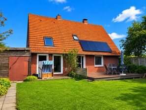 A two-story house with a red-tiled roof, a small balcony with a solar panel, a wooden deck, and a well-maintained lawn. - Enjoy a relaxing vacation at the DEICHSTERN vacation home in Butjadingen (Butjadingen)