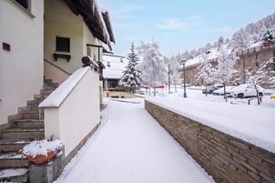 Un sendero cubierto de nieve que lleva a un edificio con un muro de piedra y un coche rojo estacionado al fondo.