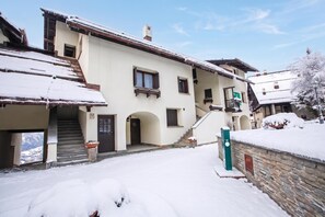 Un edificio cubierto de nieve con una escalera que lleva a la entrada, un balcón y un muro de piedra.