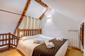 A bedroom with a sloped ceiling, a wooden bed frame, white bedding, a brown throw blanket, and a magazine on the bed. - Home Suite Grange (Sauze di Cesana)