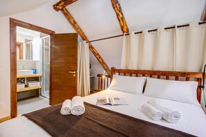 A hotel room with a wooden headboard, a bed with white linens, a brown woven mat, and a view of a bathroom with a mirror and sink. - Home Suite Grange (Sauze di Cesana)