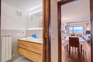 Un baño moderno con un mueble tocador de madera, un lavabo blanco y una zona de ducha.