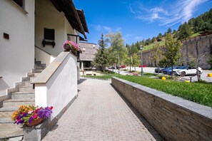 Un sendero pavimentado que conduce a un edificio con un muro de piedra y macetas con flores.
