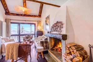 A cozy room with a fireplace, wooden beams, a large window with a view, and a wicker chair. - Home Suite Grange (Sauze di Cesana)