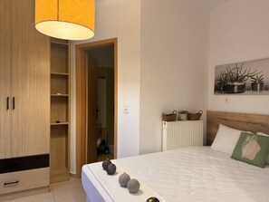 A bedroom with a bed, bedside table, lamp, wardrobe, radiator, and wall-mounted plants. - Urban Beach Sea (2D) (Rethimno)