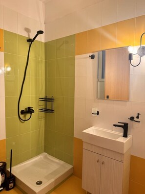 A bathroom with a shower, a sink, and a mirror. - Urban Beach Sea (2D) (Rethimno)