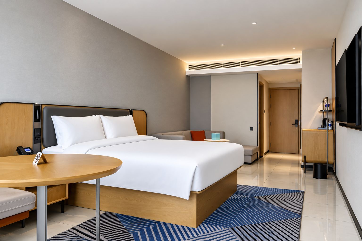 Une chambre d’hôtel moderne équipée d’un lit, d’une table de chevet et d’un téléviseur fixé au mur.