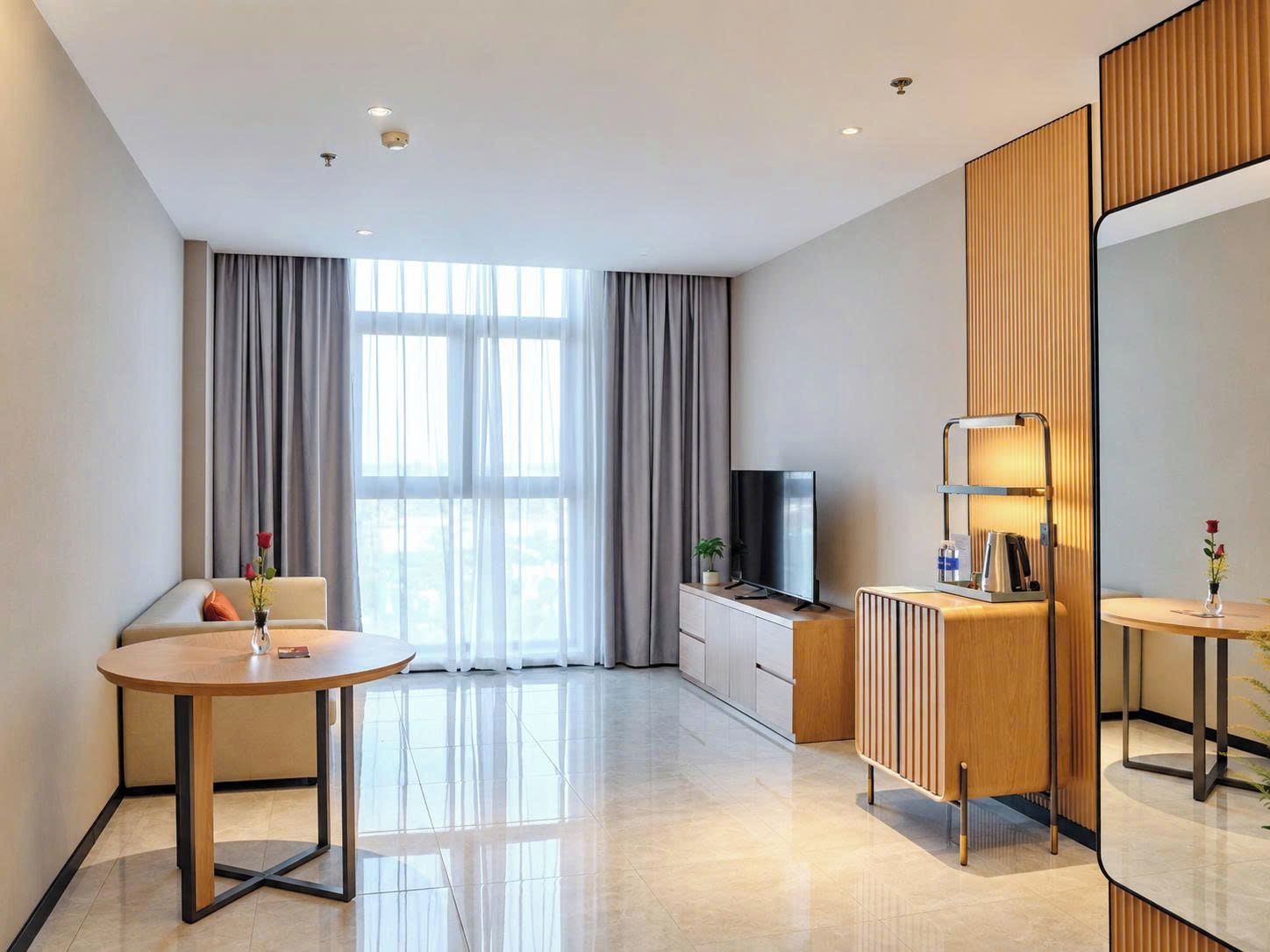 Une chambre d’hôtel moderne avec un canapé, une table ronde, un téléviseur, un radiateur et un grand miroir.