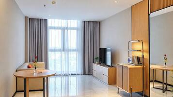 Une chambre d’hôtel moderne avec un canapé, une table ronde, un téléviseur, un radiateur et un grand miroir.