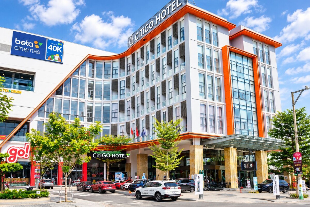 Un hotel moderno con un llamativo letrero 'CITIGO HOTEL', varios espacios de estacionamiento y un letrero de 'beta cinemas' que indica un cine cercano.