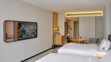 Habitación de hotel con dos camas, un escritorio, una silla, una mesita, un espejo y un televisor montado en la pared.