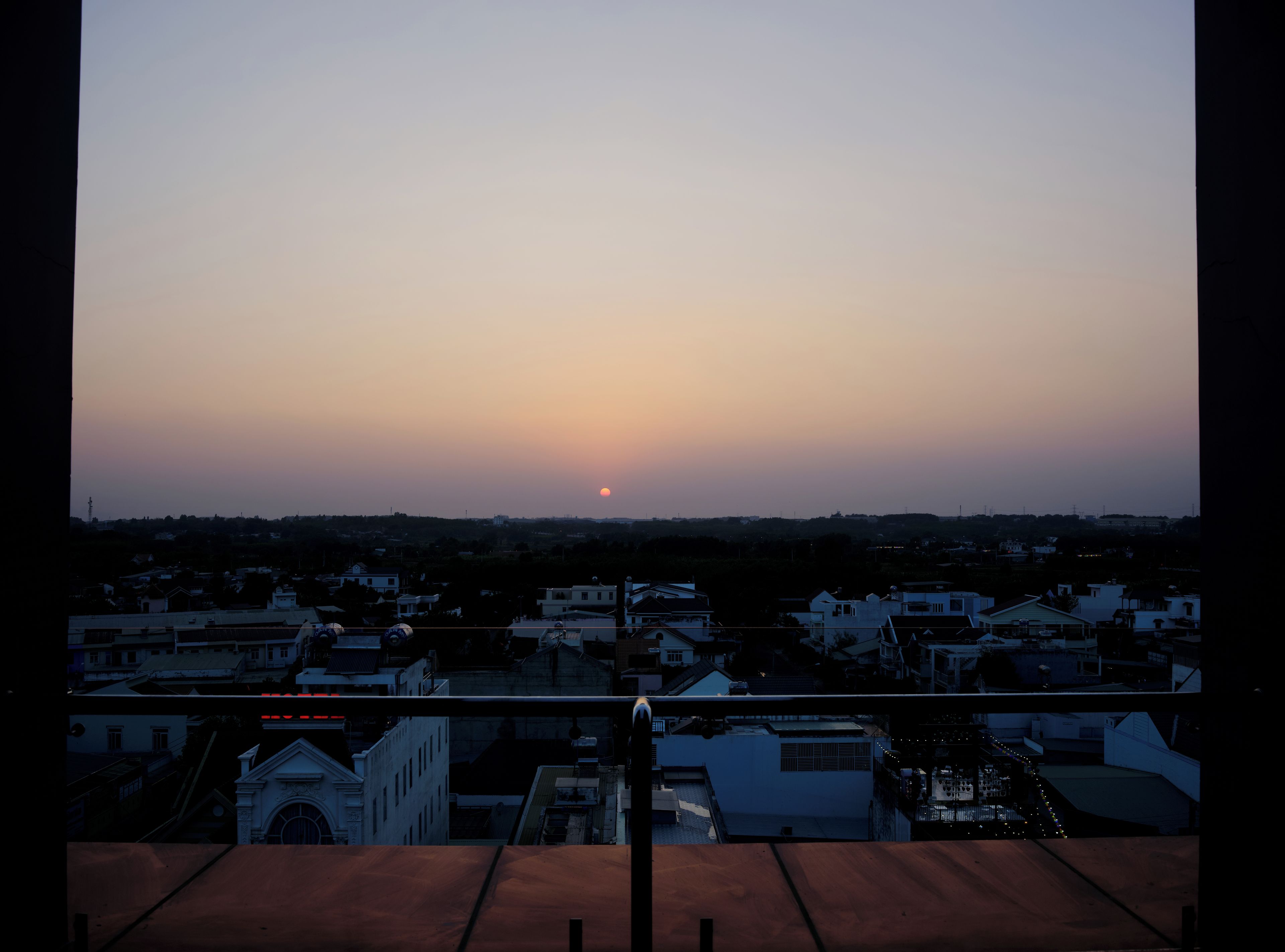Une vue sur le coucher de soleil depuis un balcon donnant sur un quartier résidentiel avec des maisons et une église.