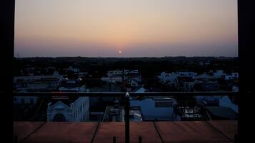 Une vue sur le coucher de soleil depuis un balcon donnant sur un quartier résidentiel avec des maisons et une église.