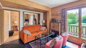 A wooden interior with a sofa, a glass coffee table, and a pink chair. - Apartment for rent near the city center. (Megève)