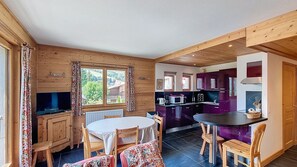 A cozy cabin interior with a dining area, kitchen, and a large window offering a view of the outdoors. - Apartment for rent near the city center. (Megève)