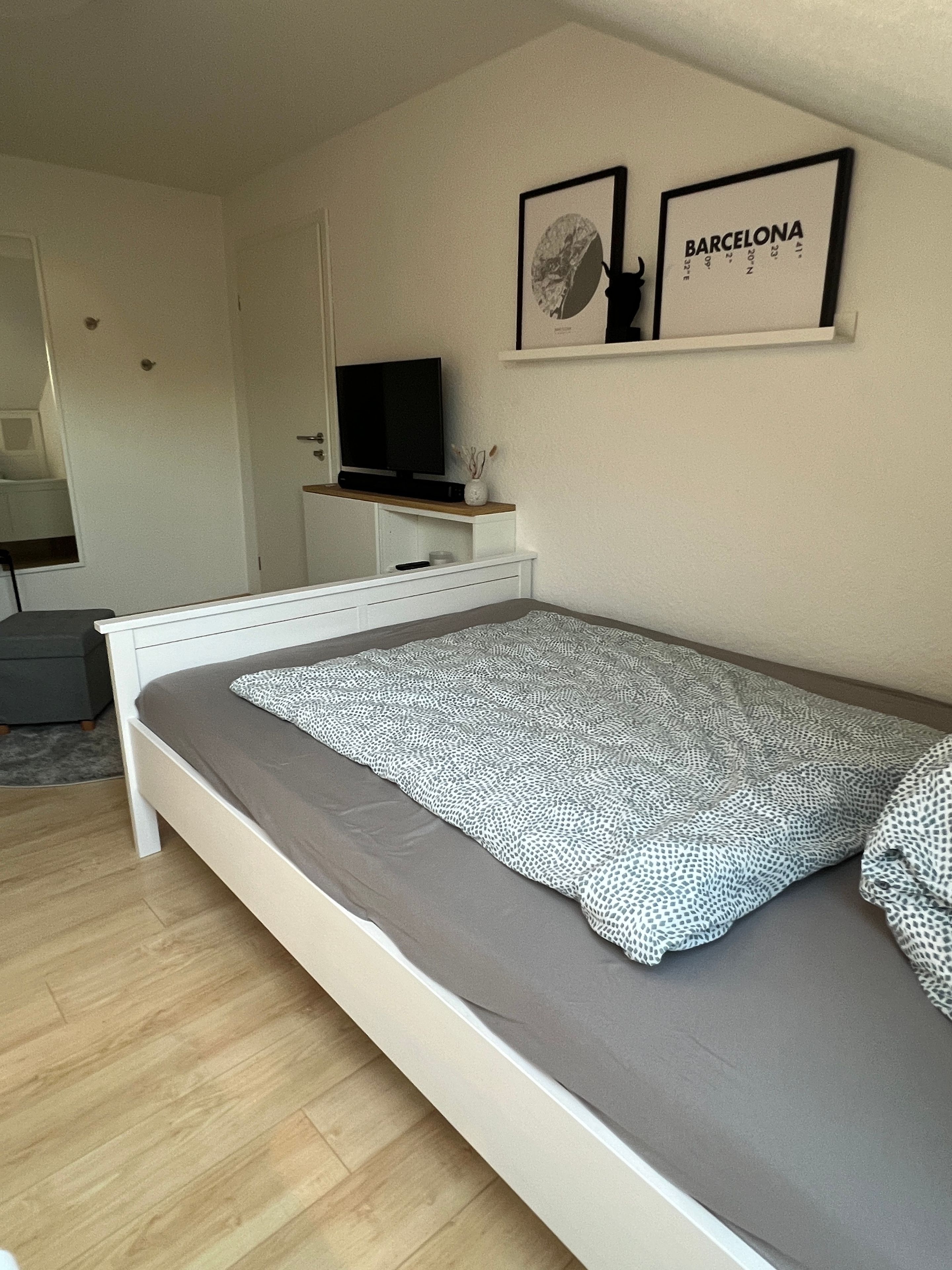 Ein Schlafzimmer mit einem Bett, einem Fernseher auf einem Schrank und zwei gerahmten Bildern an der Wand.