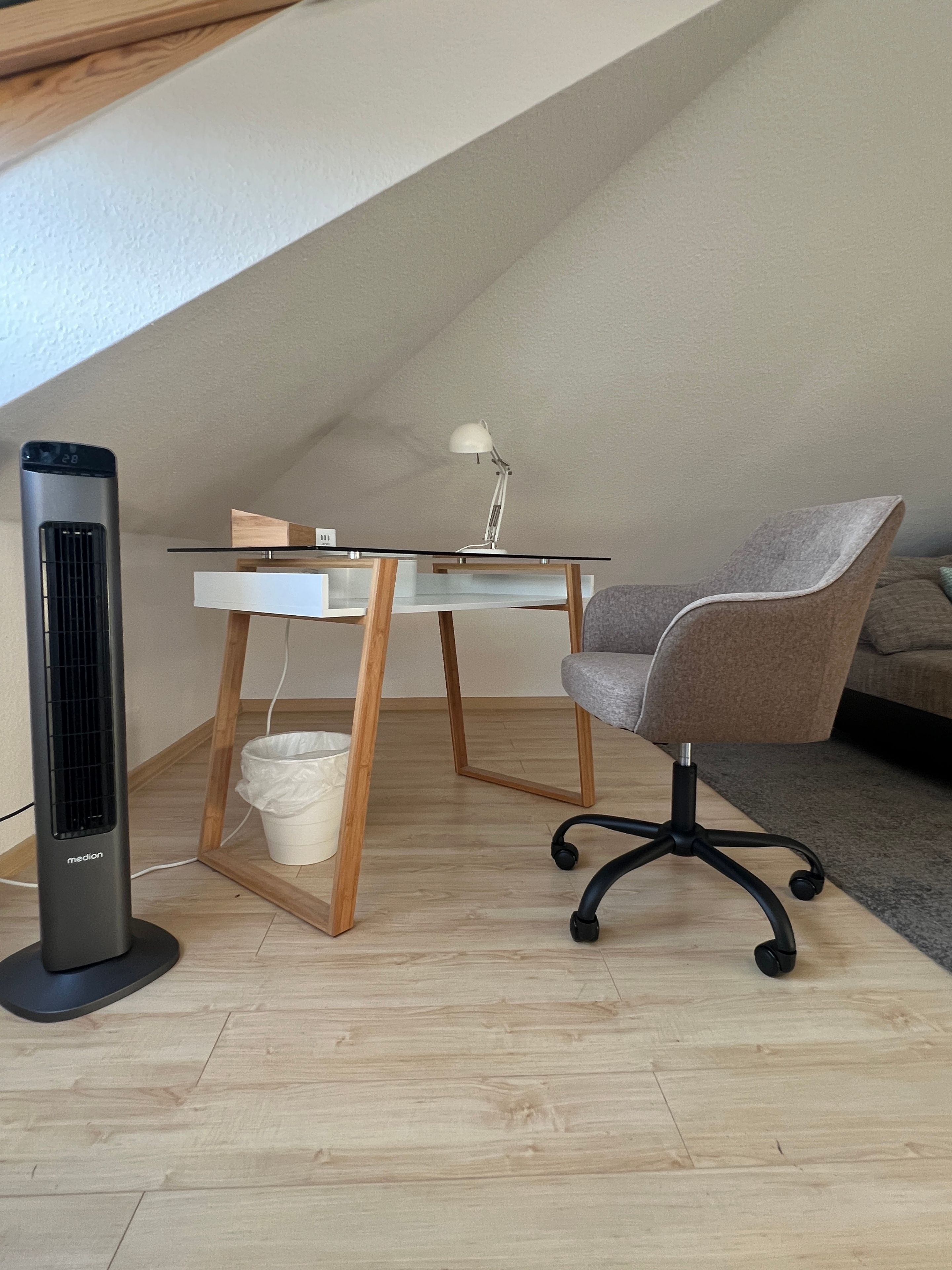 A modern office space with a standing heater, a desk with a lamp, and an ergonomic office chair.