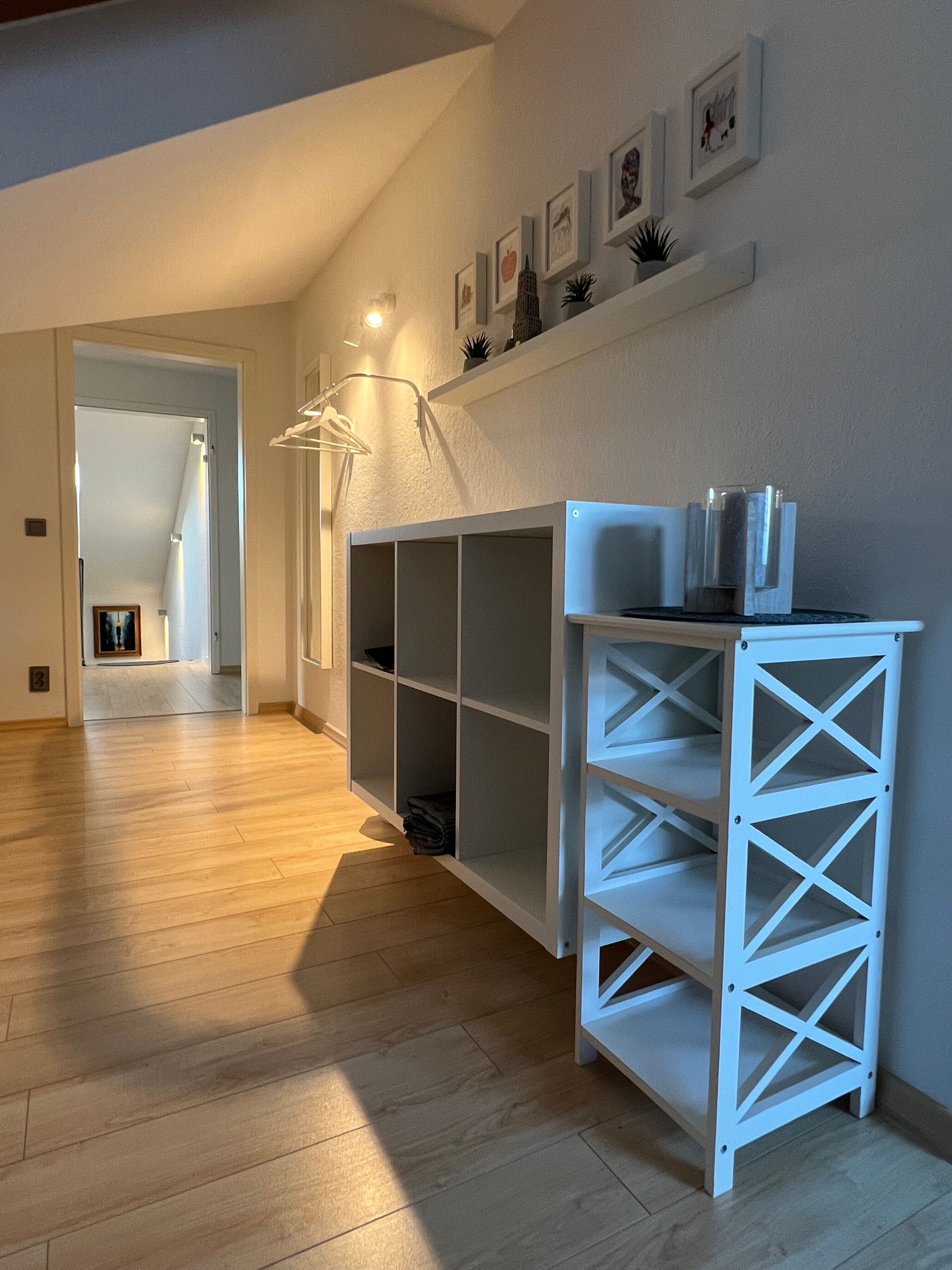A hallway with a white shelving unit, wooden flooring, and a door leading to another room.