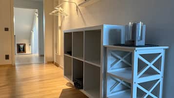 A hallway with a white shelving unit, wooden flooring, and a door leading to another room.