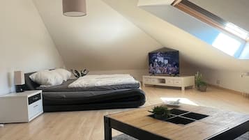 Ein modernes Schlafzimmer im Loftsstil mit schrägem Dach, einem Bett, einem Fernseher und einer kleinen Schreibtischzeile.