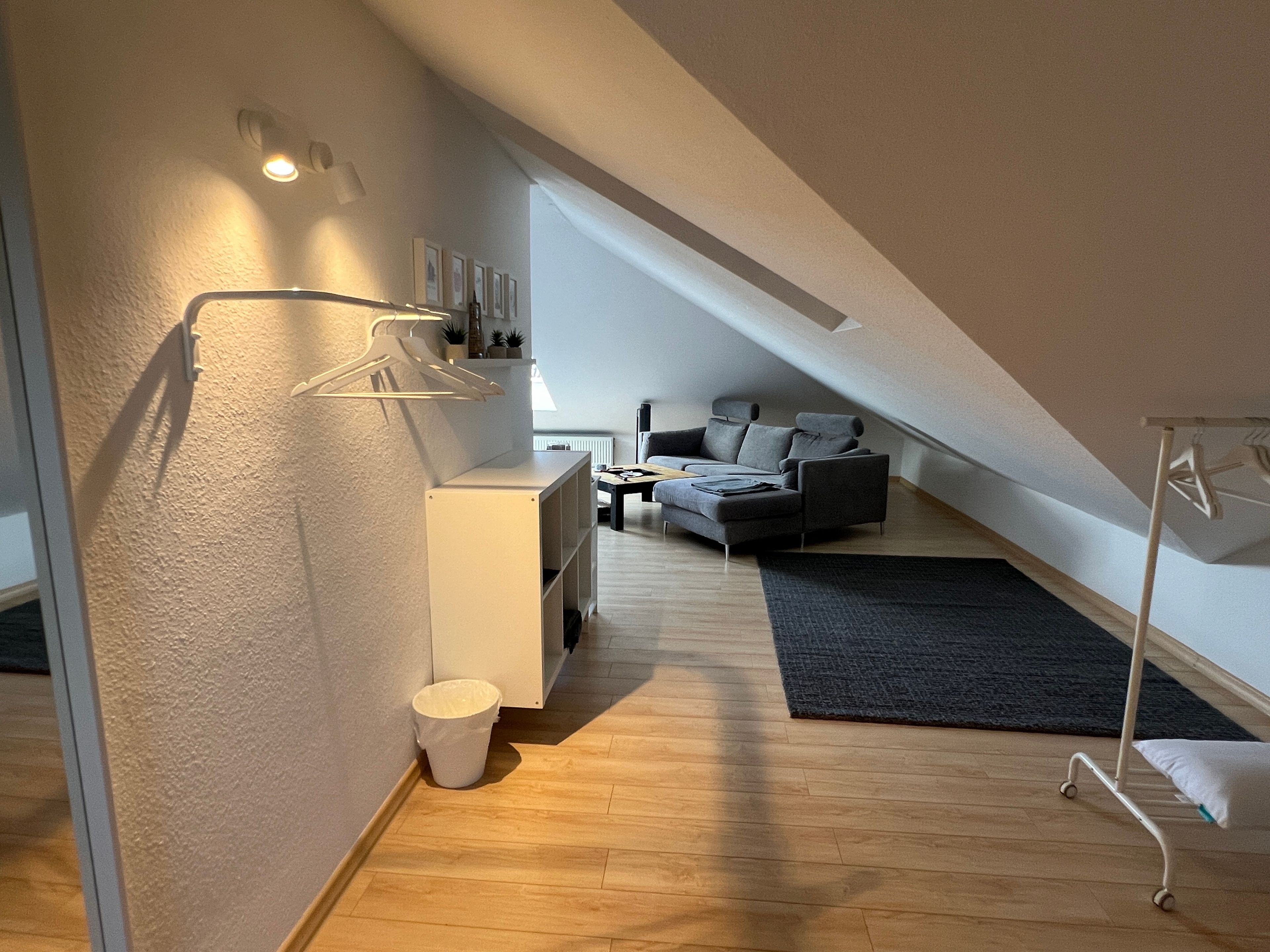 Ein modernes Schlafzimmer im Loft-Stil mit schrägverdeckter Decke, integriertem Schreibtisch, grauem Sofa und dunklem Teppich.