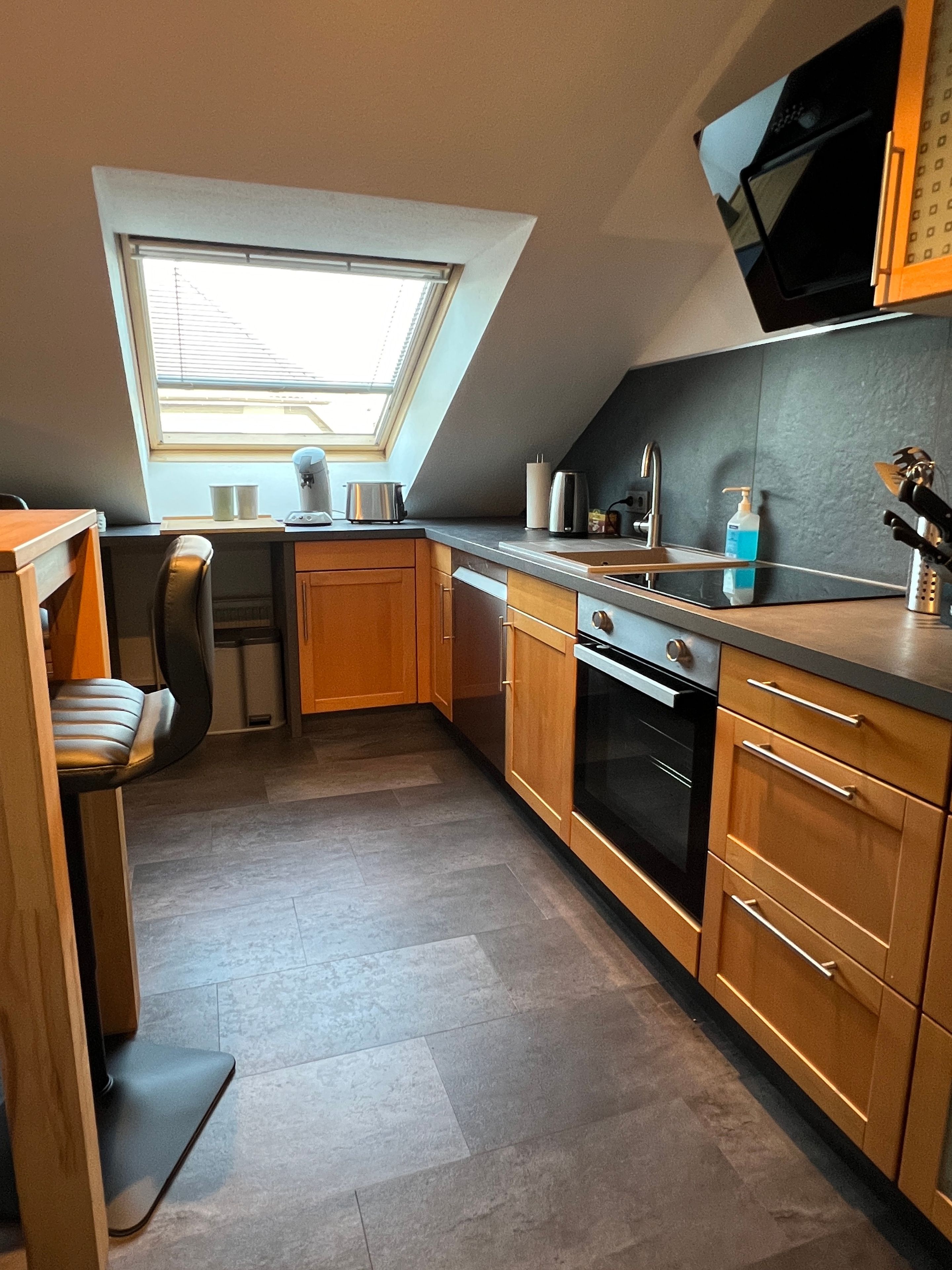 A compact kitchen with a skylight, a built-in oven, and a small dining area with a chair.