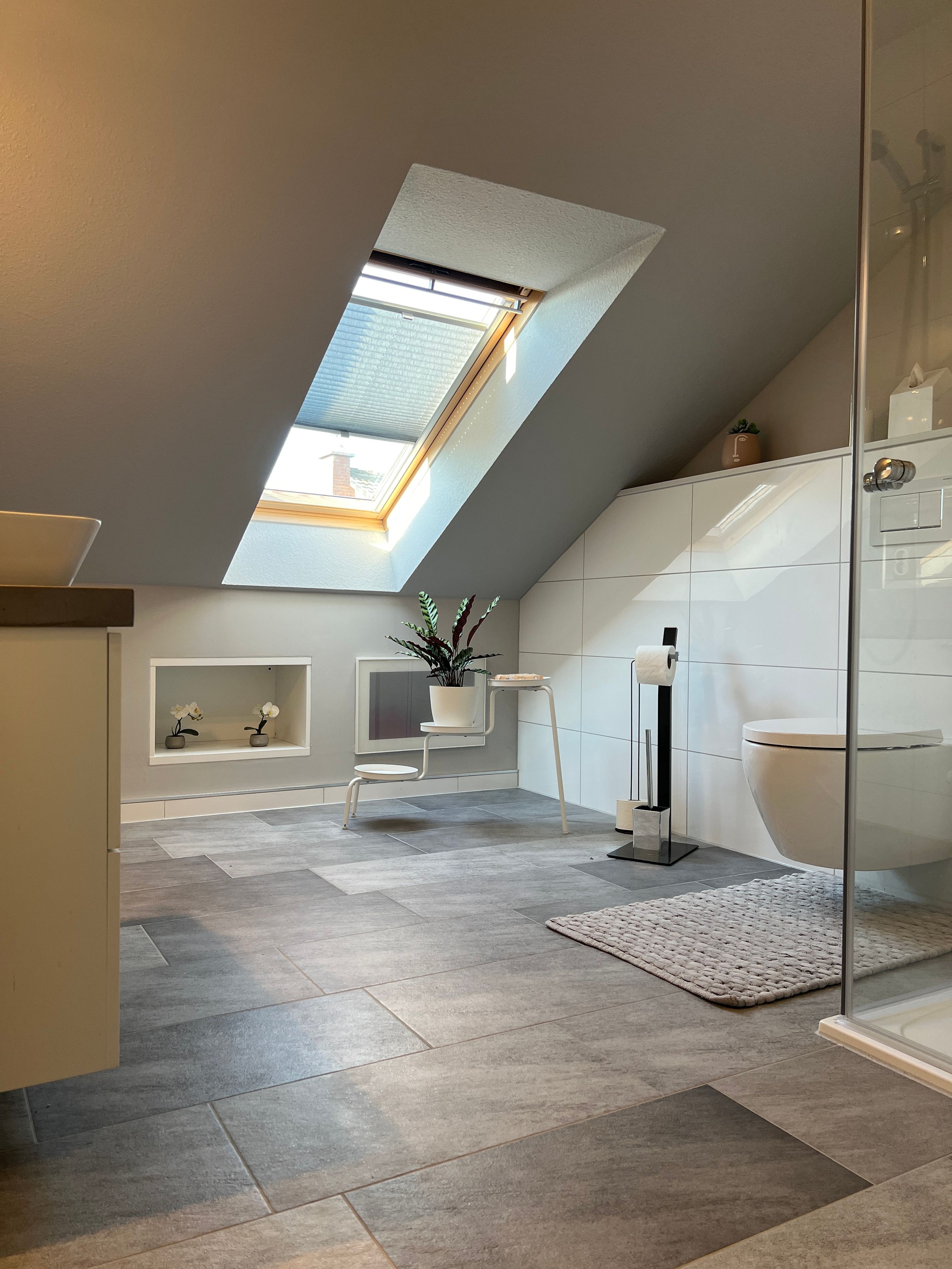 Ein modernes Badezimmer mit Dachfenster, Toilette, Waschbecken und einer kleinen Pflanze.