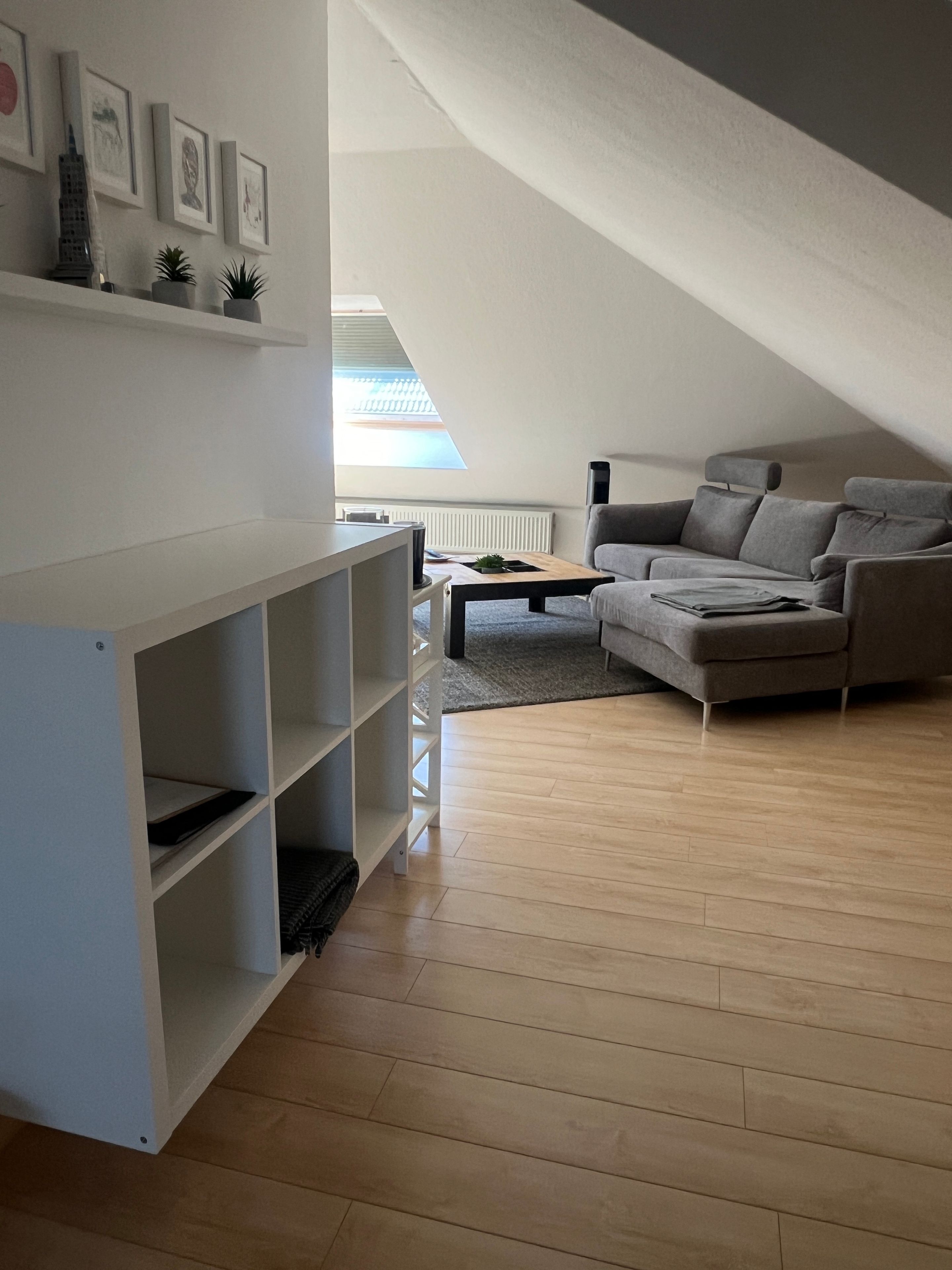 Ein modernes Wohnzimmer mit einem grauen Sofa, einer weißen Regaleinheit und Holzböden.