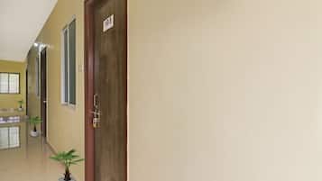 Un pasillo con puerta de madera marcada '103', plantas en macetas y piso de baldosas.