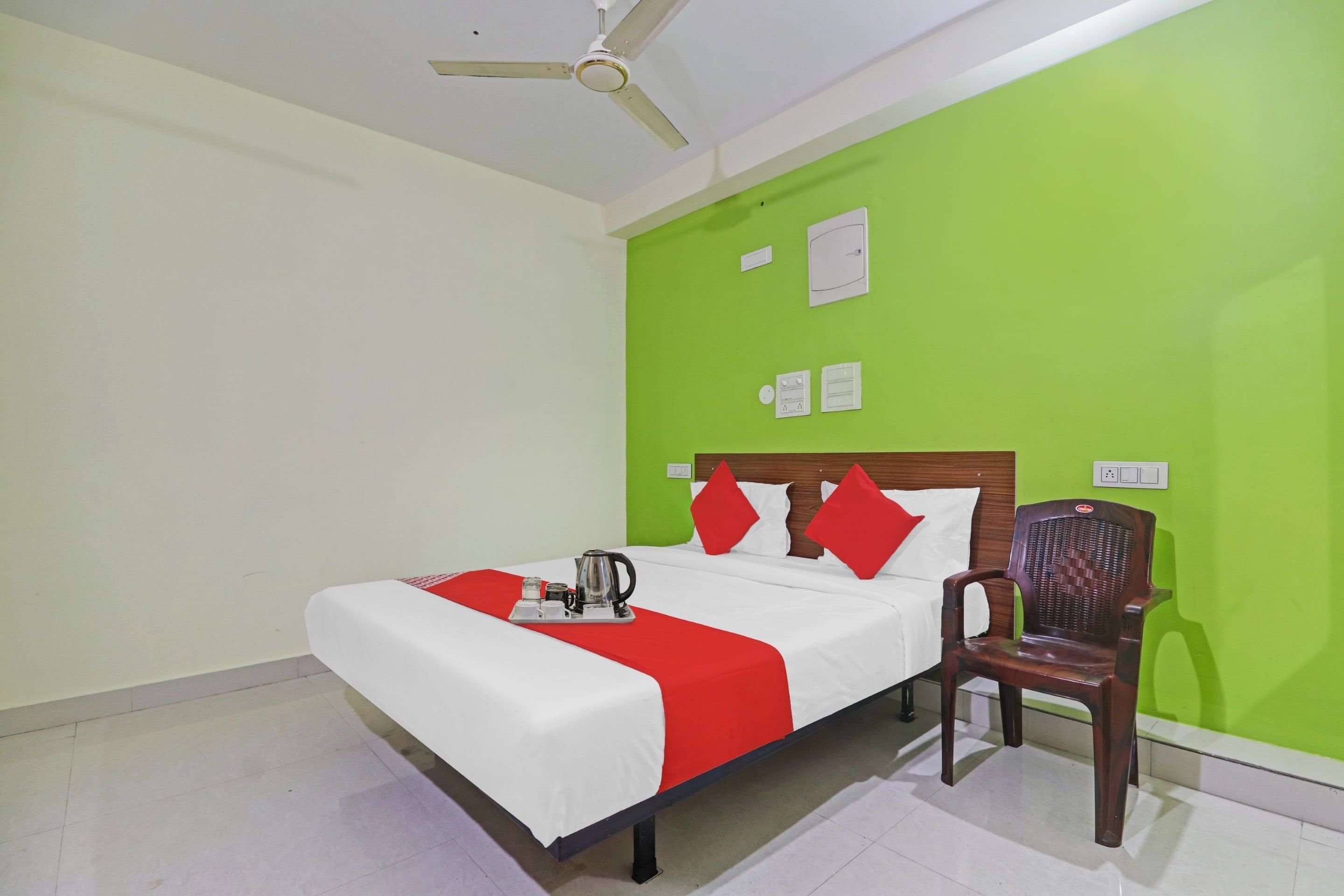 A hotel room with a bed, a chair, a ceiling fan, and a green wall.