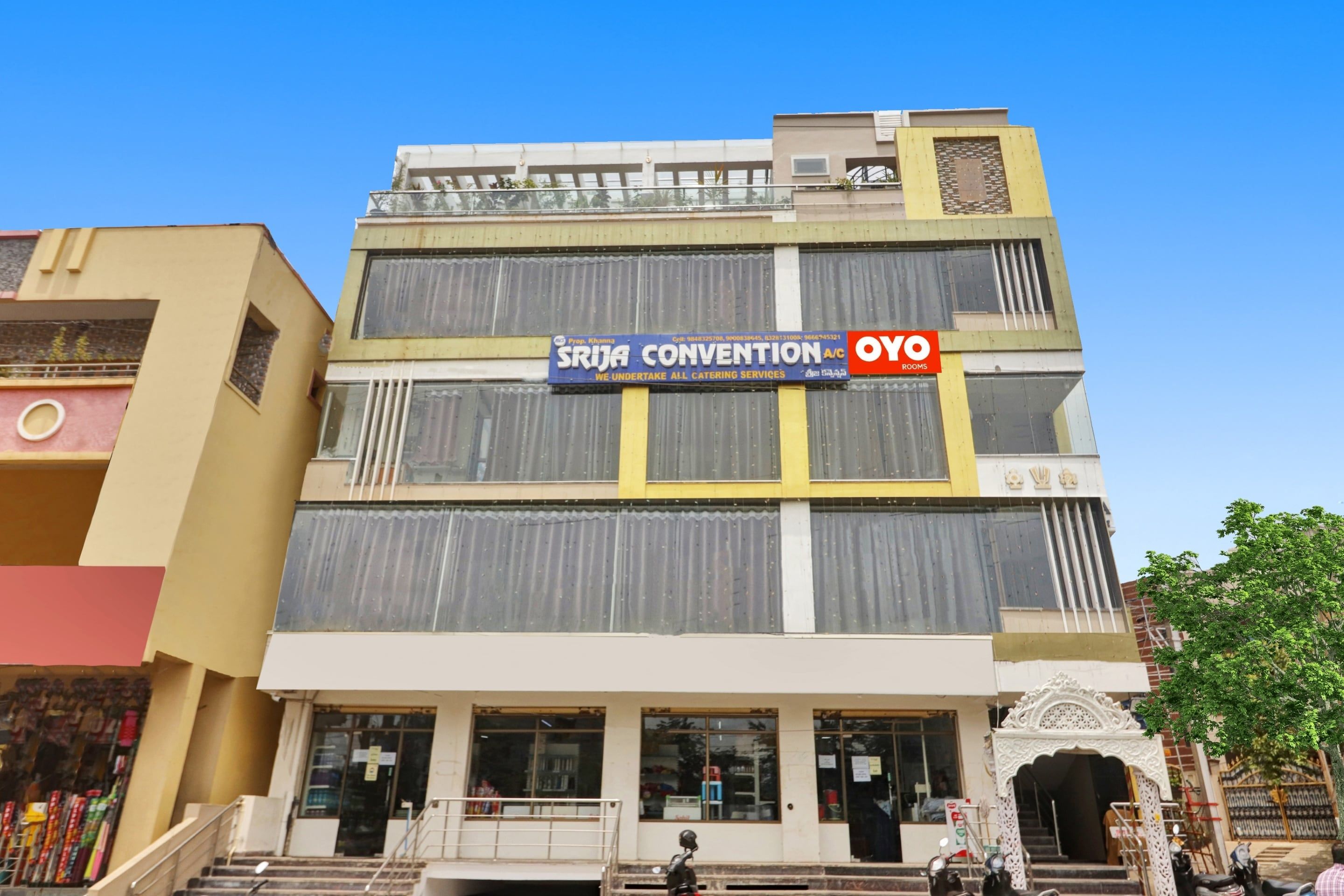 A multi-story building with a sign for 'SRJA Convention' and 'OYO Rooms' indicating a hotel or conference venue.