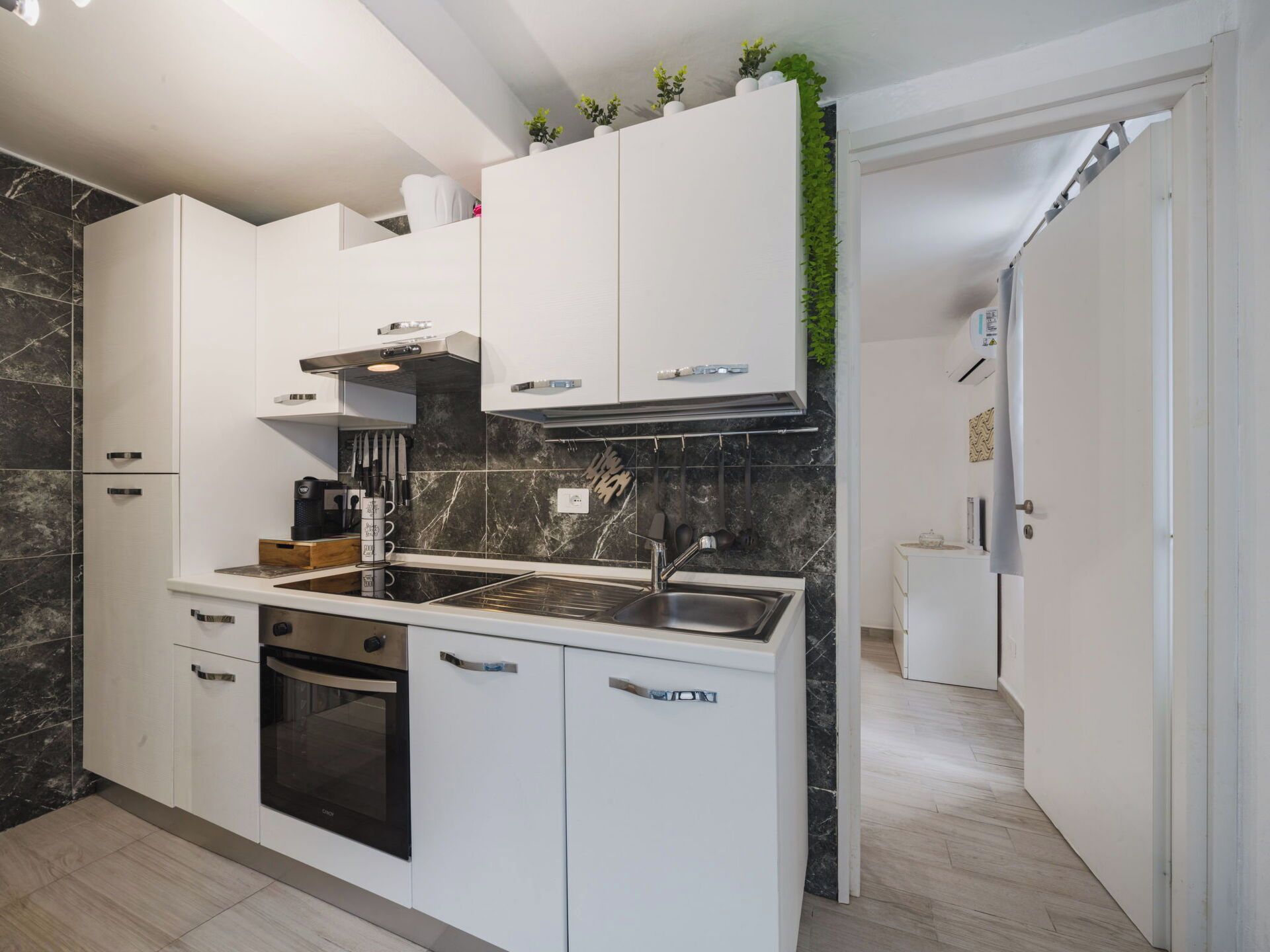 A modern kitchen with white cabinetry, a built-in oven, and a stainless steel sink.