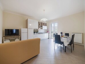 Eine moderne Küche mit weißen Schränken, ein Essbereich mit Tisch und Stühlen, ein Sofa und ein Fernseher.