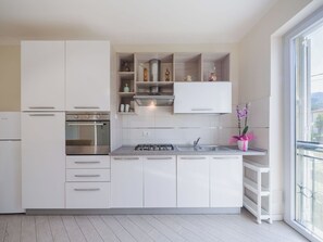 Eine moderne Küche mit weißen Schränken, einem eingebauten Ofen, einem Gaskochfeld und einem Fenster mit Blick auf einen Balkon.