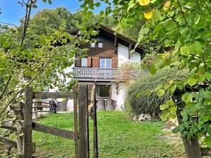 Ein zweistöckiges Haus mit Balkon, umgeben von einem Holzzaun und viel Grün.