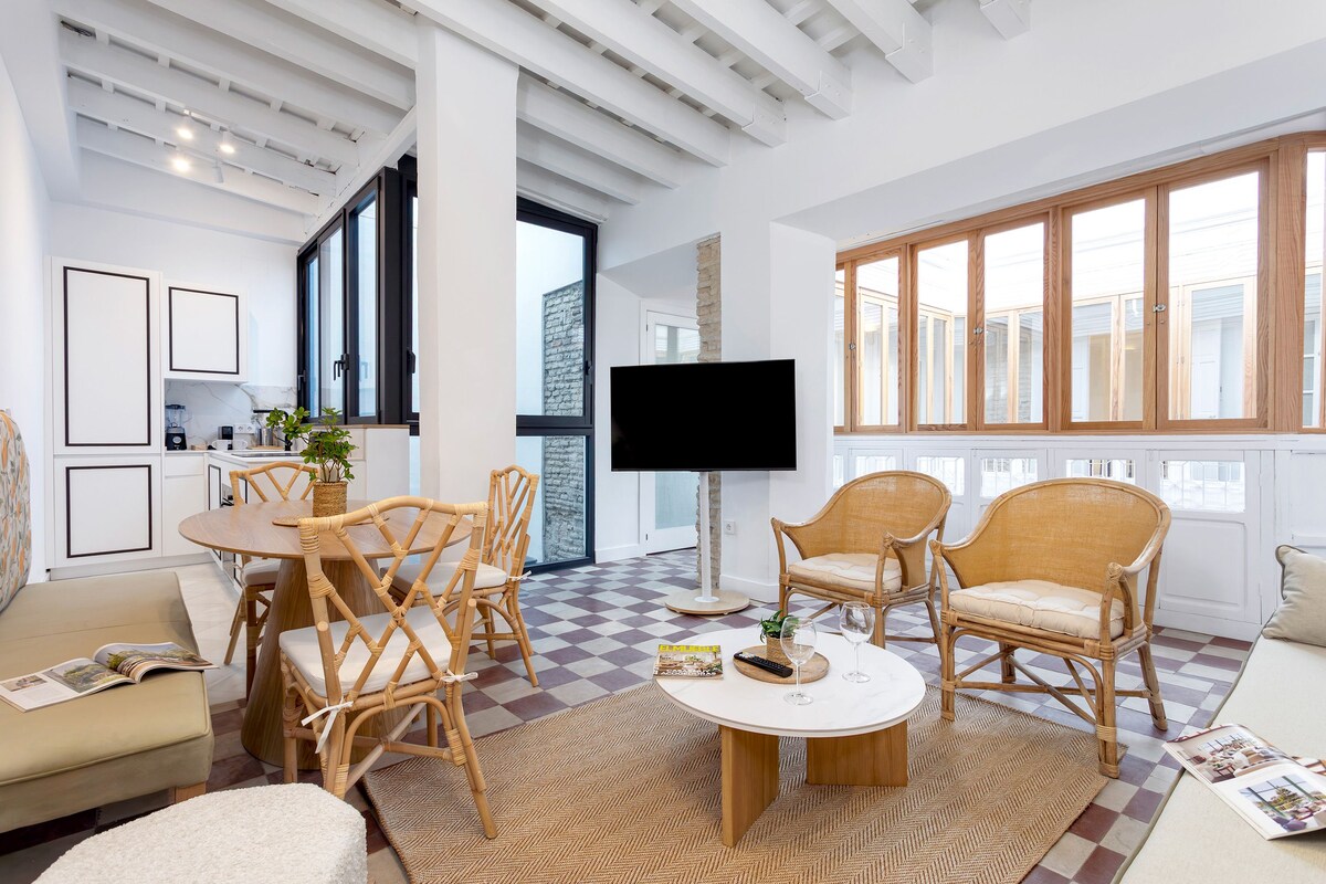 A modern living room with a dining area, large windows, and a flat-screen TV.