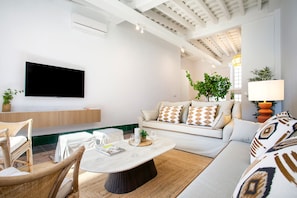 Een moderne woonkamer met een flatscreen televisie, een bank met opvallende kussens, een salontafel en een plant.