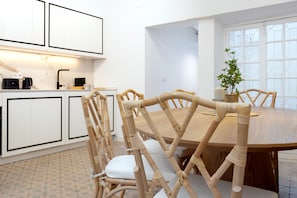 A modern kitchen with white cabinets, a black coffee machine, and a dining area with a wooden table and chairs. - Genteel Home Patio del Arenal (Seville)