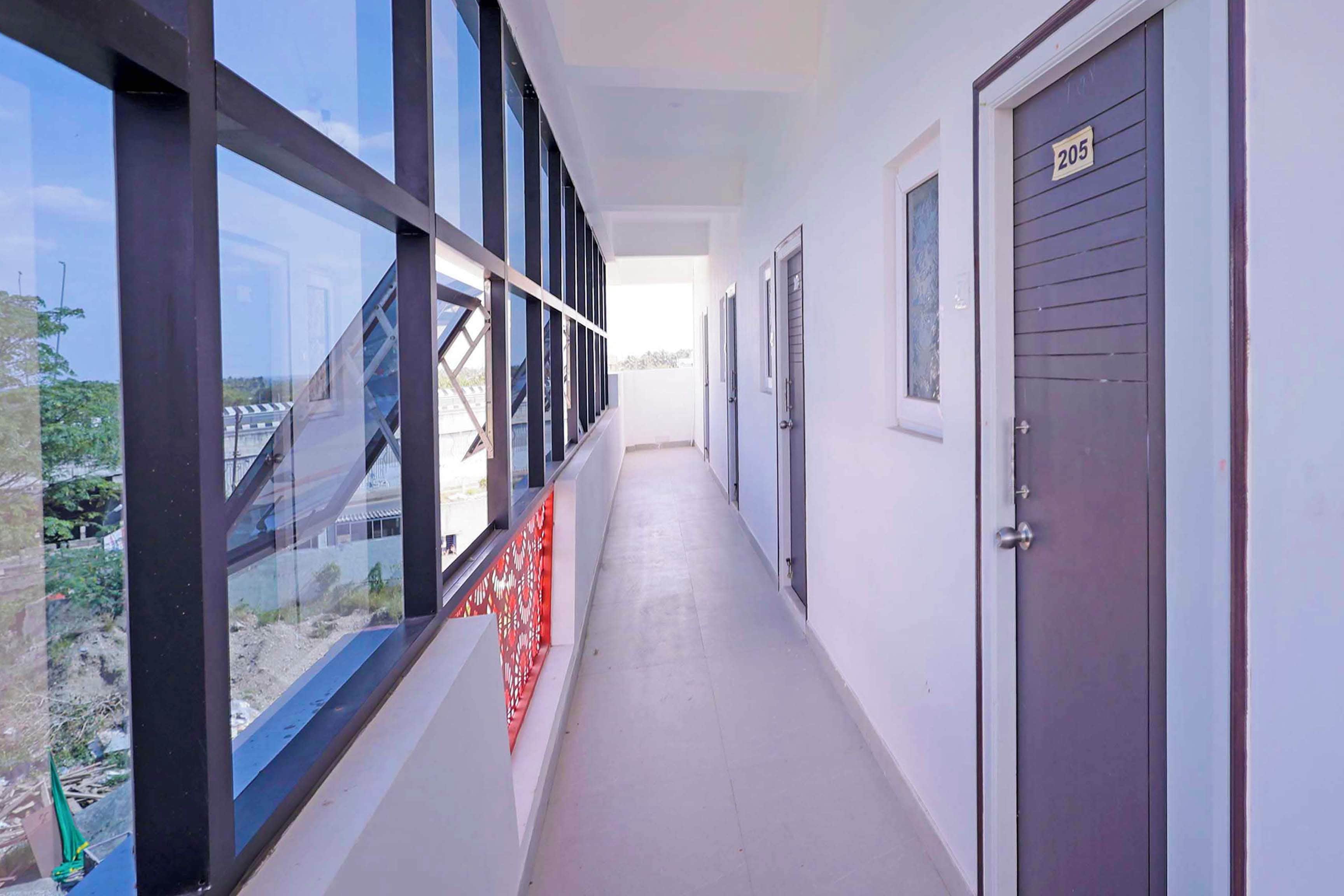 A corridor with large windows, a door marked with the number 205, and a patterned red barrier.