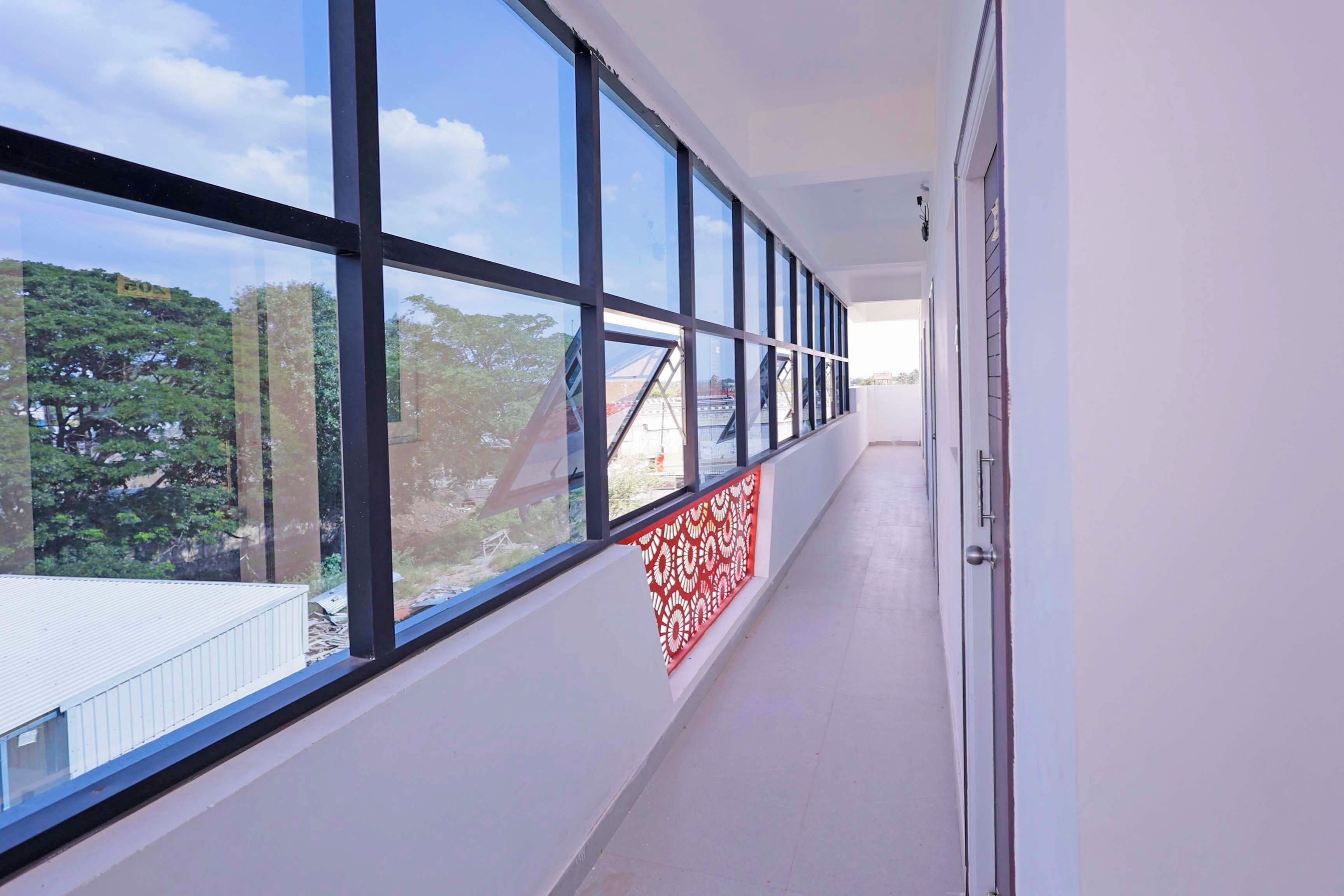 Un couloir doté de grandes fenêtres, d’un mur décoré d’un motif rouge et d’une porte située sur le côté droit.
