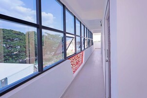 A corridor with large windows, a red patterned wall, and a door on the right.