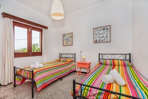 A room with two beds, a window with curtains, a small table with a lamp, and two wall-mounted pictures. - Villa Sureda - By Dream Villas Pollensa (Pollensa)