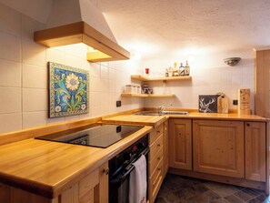 Eine Küche mit Holzausstattung, integriertem Backofen, Spüle und dekorativer Fliesenrückwand.