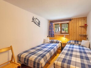 Ein Zimmer mit zwei Betten, einem Holzkopfende, einem kleinen Tisch, einer Wanddekoration und einem Fenster mit Vorhängen.