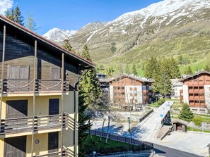 Un pueblo de montaña con edificios tradicionales de madera, cielo despejado y montañas nevadas al fondo.